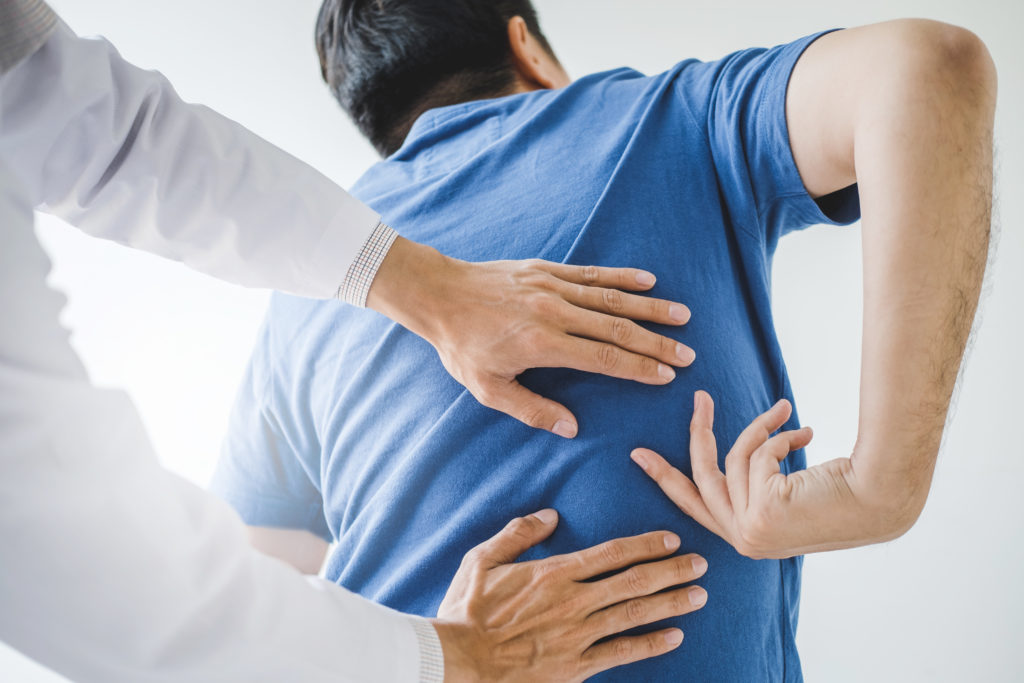 A physician examines a man's back following a back injury