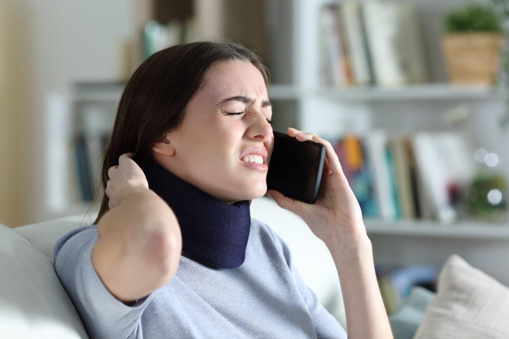 A woman wearing a neck brace contacts a personal injury attorney on her phone