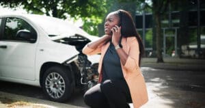 Worried woman on the phone next to a damaged car after an uninsured driver car accident