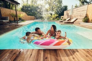 Family playing in a swimming pool in a fenced backyard